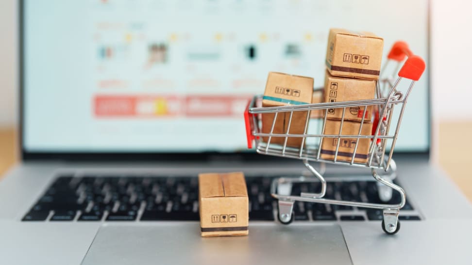 A miniature shopping cart sits on the keyboard of a laptop