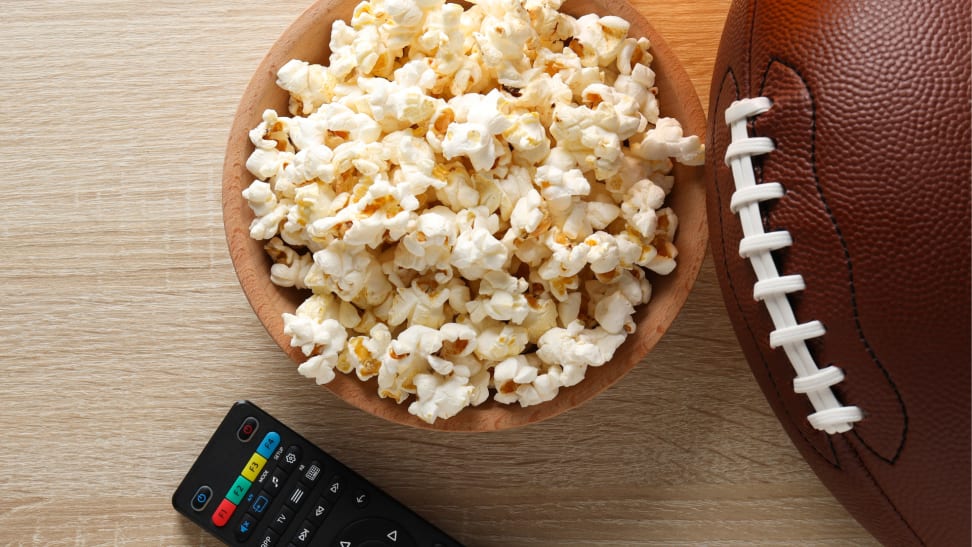 A bowl of popcorn on a table with a football and TV remote