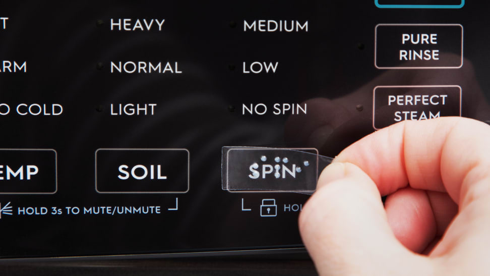 A hand places a braille label over the spin function of a washing machine