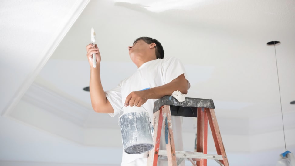 Person on ladder painting the ceiling white with a brush
