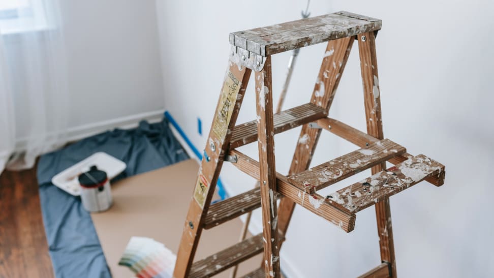 A paint-splattered ladder and drop cloth next to a white wall