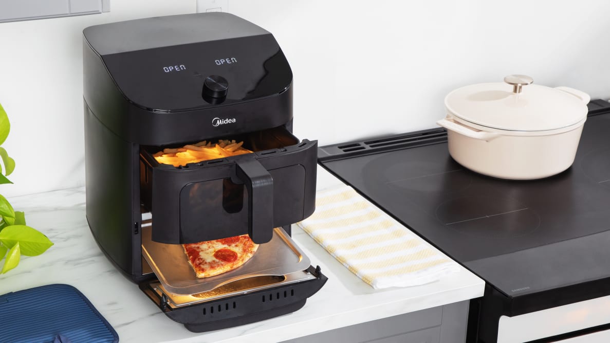 Midea air fryer on a kitchen counter with pizza cooking in bottom section and fries cooking in top basket