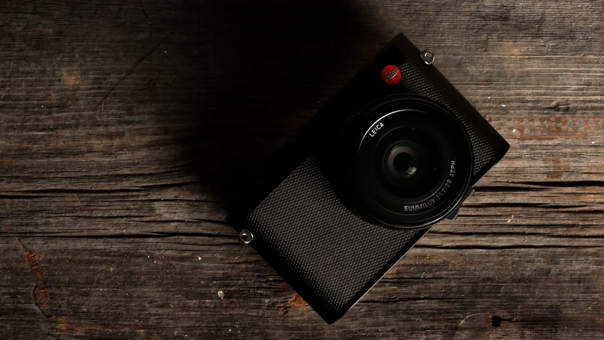 A black Leica Q (Typ 116) camera sits on a wooden table facing up