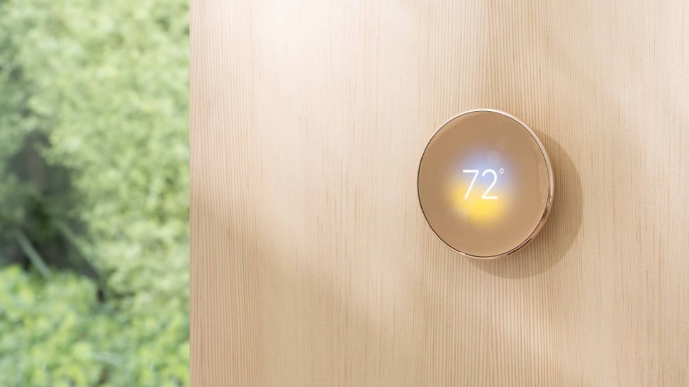 The fourth-gen Nest Learning Thermostat shown in gold hangs on a wood wall.
