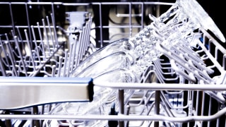 A close-up of a dishwasher's upper rack, showing wine glasses resting in stemware holders.